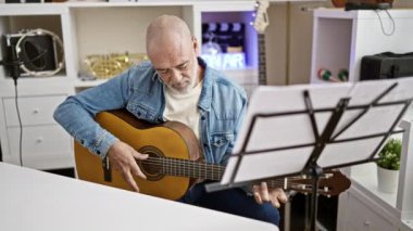 Odaklanmış son sınıf öğrencisi, müzik aletleriyle birlikte bir ev stüdyosunda gitar çalıyor..