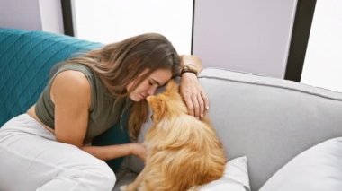 Kendine güveni tam, İspanyol bir kadın evdeki kanepede köpeğiyle samimi bir öpücükten zevk alıyor, neşeli bir gülümseme sergiliyor.
