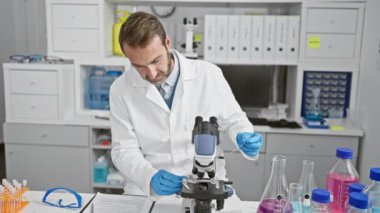 Sakallı bilim adamı laboratuvar ortamında mikroskop kullanarak örnekleri inceliyor..