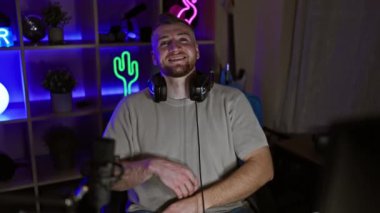 Gülümseyen sakallı bir adam, geceleri neon ışıklı bir odada oyun masasında kulaklık takıyor..