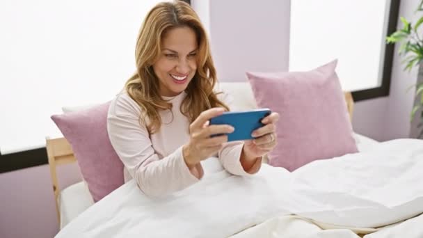 Uśmiechnięta Kobieta Bawi Się Smartfonem Łóżku Jasnej Sypialni Nowoczesnym Pastelowym — Wideo stockowe