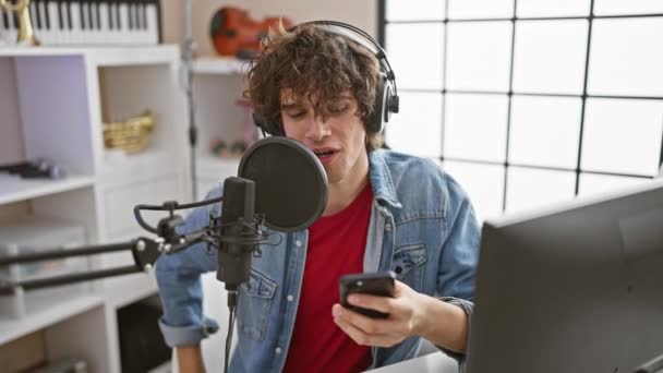Młody Mężczyzna Kręconymi Włosami Śpiewający Podczas Noszenia Słuchawek Studiu Muzycznym — Wideo stockowe