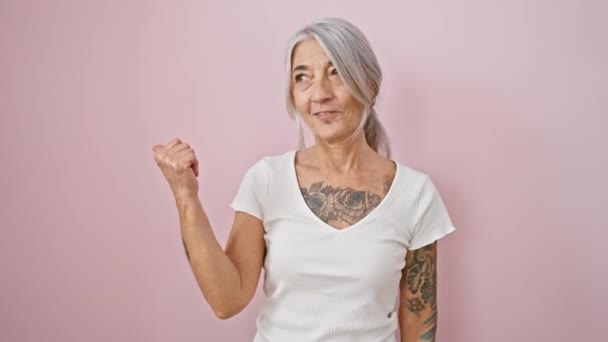 灰色の髪を持つ自信を持った中年の女性は陽気で立って 親指を大きく笑わせ 孤立したピンクの背景の上に楽観主義を語ります — ストック動画