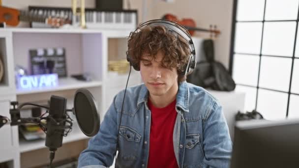 Młody Mężczyzna Kręconymi Włosami Dżinsową Kurtką Nagrywa Wokal Nosząc Słuchawki — Wideo stockowe