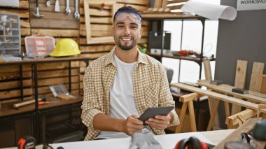 Modern marangozluk atölyesinde güvenlik gözlüğü takan sakallı yakışıklı bir adam.