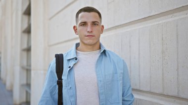 Gündelik kıyafetli, kendine güvenen, üniversite kampüsünde duran genç bir İspanyol..