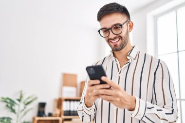 Genç İspanyol iş adamı ofisteki akıllı telefonu kullanarak gülümsüyor.