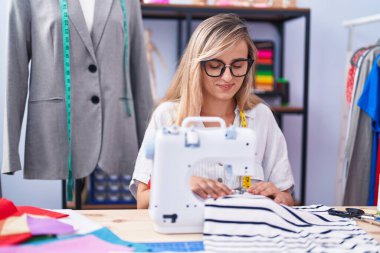Terzide dikiş makinesi kullanan kendine güvenen genç sarışın kadın terzi.