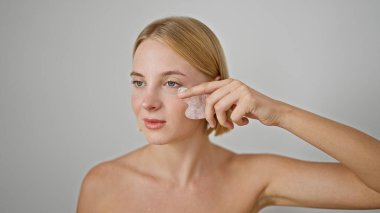 Genç sarışın kadın pembe kuvars gua kullanarak yüz masajı yapıyor.