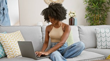 African american woman using laptop sitting on sofa at home