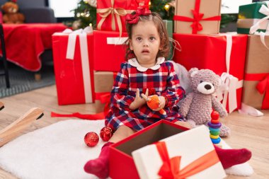 Sevimli sarışın bebek elinde oyuncakla evde Noel ağacının yanında oturuyor.