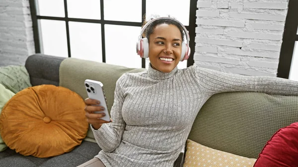 Smiling woman with headphones using smartphone in cozy living room interior