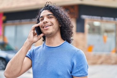 Genç Latin adam gülümsüyor. Kendine güveniyor. Akıllı telefondan konuşuyor.