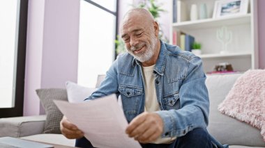 Sakallı, gülümseyen, rahat bir oturma odasında gazete okuyan, rahat ve rahat bir atmosferi olan yaşlı bir adam..