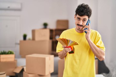 Young caucasian man holding test color talking on smartphone at new home