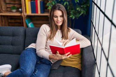 Evdeki kanepede oturmuş kitap okuyan güzel İspanyol kadın.