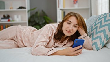 Yatak odasında akıllı telefon kullanan genç bir kadın.
