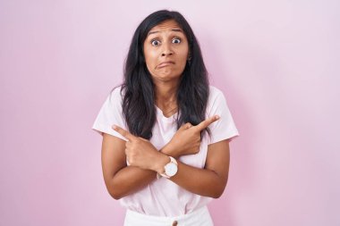 Pembe arka planda duran genç İspanyol kadın her iki tarafı da parmaklarıyla işaret ediyor. Farklı yönler farklı. 