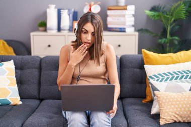 Evde çalışan genç İspanyol kadın operatör kulaklığı takıyor ağzı elle kapatıyor, şok geçiriyor ve hata yapmaktan korkuyor. şaşırmış ifade 