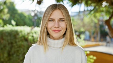 Çekici sarışın kadın, mavi gözlü, yemyeşil bir bahçede beyaz giyen.