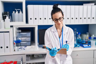 Young caucasian woman scientist smiling confident writing on notebook at laboratory