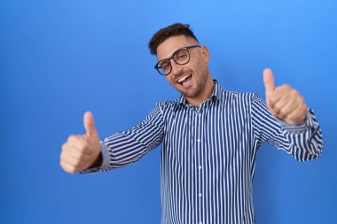 Sakallı, gözlüklü İspanyol adam elleriyle olumlu jest yapıyor, gülümsüyor ve başarı için seviniyor. kazanan jest. 