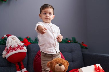 Evdeki Noel süslemesiyle koltukta kendinden emin gülümseyen sevimli İspanyol çocuk.