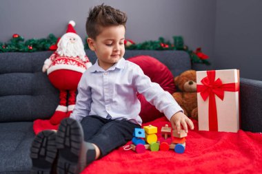 Sevimli İspanyol bebek, evdeki Noel süslemesinde koltukta oturmuş oyuncak trenle oynuyor.