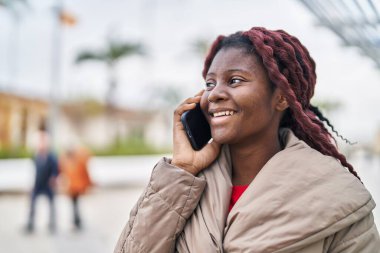 Afro-Amerikalı kadın gülümsüyor. Parktaki akıllı telefondan konuşuyor.