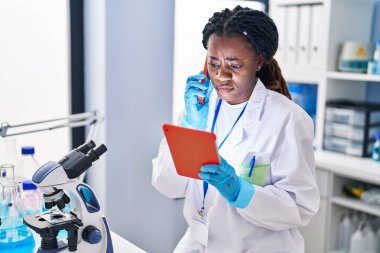 African american woman scientist talking on smartphone using touchpad at laboratory