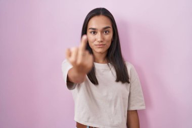 Young hispanic woman standing over pink background showing middle finger, impolite and rude fuck off expression 