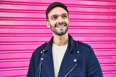 Young hispanic man smiling confident looking to the side over isolated pink metalic background