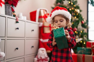 Sevimli beyaz kız elinde hediyeyle Noel ağacının yanında duruyor.