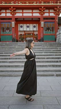 Gözlüklü neşeli İspanyol kadın, özgürlüğü kucaklıyor, gülümsüyor ve Kyoto, Japonya 'daki fushimi inari taisha türbesine bakıyor.