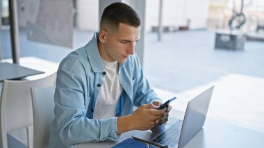 Modern üniversite kütüphanesinde bilgisayar ve akıllı telefonla çalışan yakışıklı bir İspanyol..