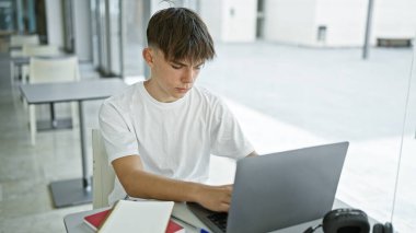 Genç beyaz bir erkek, modern bir üniversite sınıfında dizüstü bilgisayarla çalışıyor..