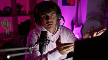 Çekici İspanyol genç adam gecenin karanlığında, derin bir sohbetin içinde, oyun kulaklığı takılı, dijital eğlenceye dalmış, karanlık oyun odasında oturuyor..