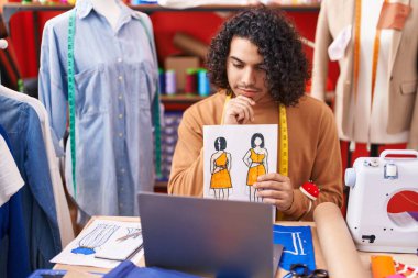 Young latin man tailor having video call showing clothing design at atelier