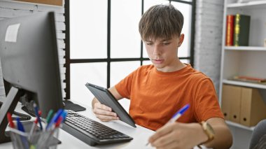 Kafkasyalı genç bir erkek öğrenci, üniversite kütüphanesi masasında tabletle çalışıyor, ciddi ve odaklanmış..