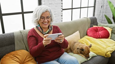 Gülümseyen gri saçlı kadın gözlükleri akıllı telefon köpek koltuğu yastıkları oturma odası yastıkları