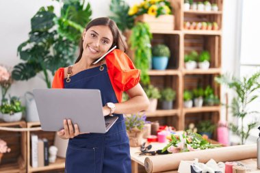 Çiçekçide dizüstü bilgisayar kullanarak konuşan güzel İspanyol çiçekçi kadın.