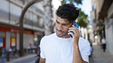 Yakışıklı İspanyol adam güneşli şehir caddesinde akıllı telefon kullanıyor.