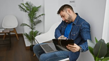 Yakışıklı İspanyol adam. Bekleme odasında laptopla, panoyla ve telefonla birden fazla iş yapıyor.