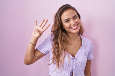 Pembe arka planda duran genç İspanyol kadın dört numarayı gösterip işaret ederken kendinden emin ve mutlu bir şekilde gülümsüyor.. 