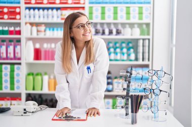 Young beautiful hispanic woman pharmacist smiling confident writing on document at pharmacy