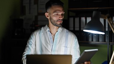 Genç İspanyol iş adamı dokunmatik ped ve dizüstü bilgisayar kullanarak ofise gülümsüyor.