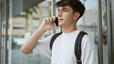 Sırt çantasıyla önemli bir telefon görüşmesi yapmak için akıllı telefonu kullanan sıradan bir İspanyol üniversite öğrencisi. Güneşli şehir kampüsünde durmuş, sohbete dalmış..