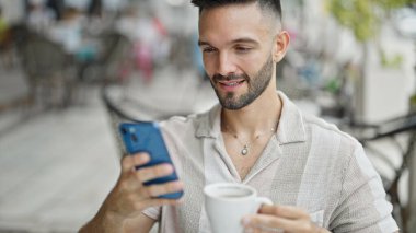 Genç İspanyol adam akıllı telefon kullanıyor. Kahve dükkanının terasında kahve içiyor.