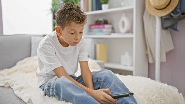 Sevimli sarışın çocuk sıkılmış bir ifade takınıyor, evdeki kanepede rahatça kıvranıyor, rahatlarken ciddi görünüyor ve oturma odasında televizyon seyrediyor.