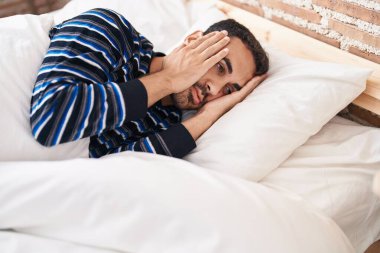 Young hispanic man stressed lying on bed at bedroom